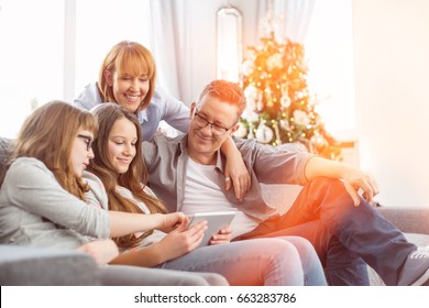 Family Using Tablet PC On Sofa With Christmas Tree In Background