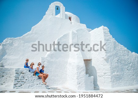 Family vacation in Europe. Parents and kids at street of typical greek traditional village with white walls and colorful doors on Mykonos Island
