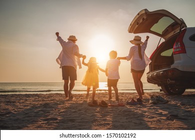 Family Vacation Holiday, Happy Family Running On The Beach In The Evening. Back View Of A Happy Family On A Tropical Beach And A Car On The Side. Mother, Father, Children On The Sea At Sunset. 