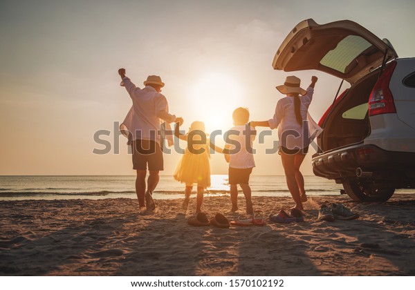Family vacation holiday, Happy family running on the\
beach in the evening. Back view of a happy family on a tropical\
beach and a car on the side. Mother, father, children on the sea at\
sunset. 