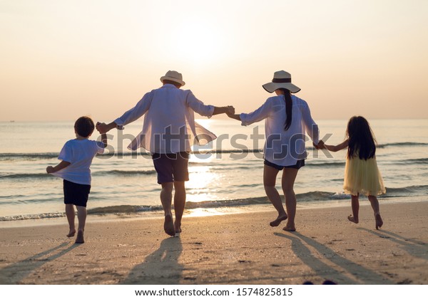 Family vacation holiday, Happy family running on\
the beach in the evening. Back view of a happy family on a tropical\
beach and a car on the side. Mother, father, children on the sea at\
sunset.