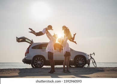 Family Vacation Holiday, Silhouette Of The Happy Family On The Evening Beach. Father And Mother Are Happily Carrying Their Son And Daughter On The Beach, Car And Bicycles In The Back.