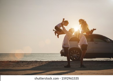 Family Vacation Holiday, Silhouette Of The Happy Family On The Evening Beach. Father And Mother Are Happily Carrying Their Son And Daughter On The Beach, Car And Bicycles In The Back.