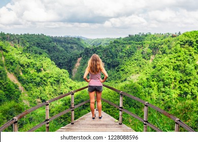 Family Vacation Lifestyle. Young Woman Stand On Edge Of Overhanging Bridge On High Cliff. Happy Girl Looking At Stunning Tropical Jungle View. Tukad Melangit Is Popular Travel Destination In Bali.