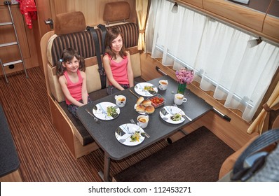 Family Vacation, RV Holiday Trip, Camping. Happy Smiling Kids Travel On Camper. Children Eating In Motorhome Interior