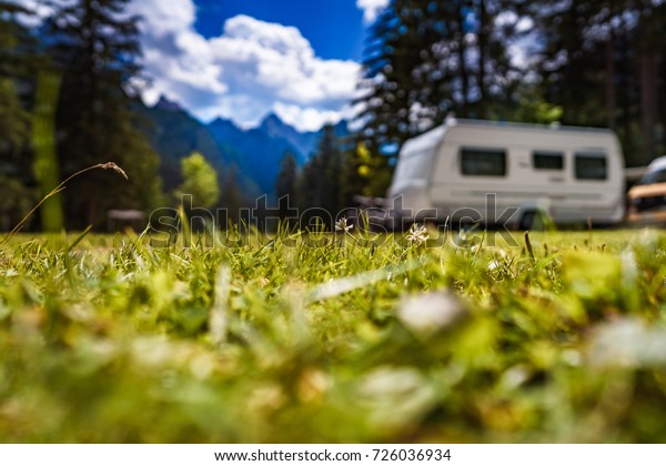 Family vacation travel,\
holiday trip in motorhome, Caravan car Vacation. Beautiful Nature\
Italy natural landscape Alps. The background is blurred, focus on\
the grass