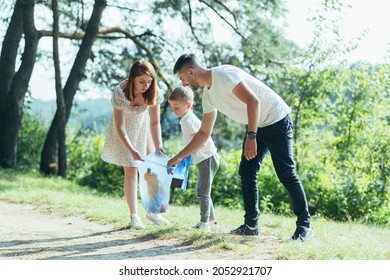 family volunteer cleans garbage in nature. Father and mother, parents, children, son family volunteers in a sunny day cleaning up the rubbish waste bottles in forest of debri folding in plastic bag - Powered by Shutterstock