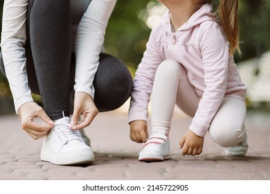 Family walk and fit sport training. Cropped close up shot of legs of sporty mother and little daughter adjusting sneakers, sitting on the jogging track in the park - Powered by Shutterstock