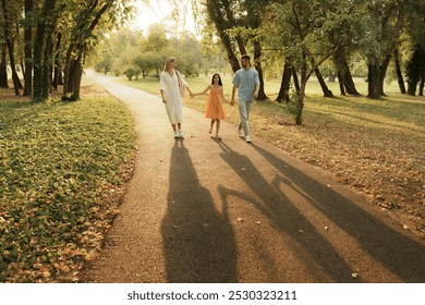 Family walking hand in hand through a sunlit park in autumn. - Powered by Shutterstock