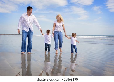 Family Walking On A Beach, All Wearing Jeans And White Shirts