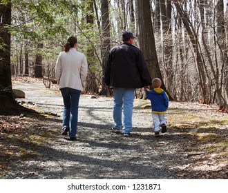 Family Walking On A Rocky Path In The Woods In  Early Spring Or Autumn.  There Are 3 People: Mother, Father, And Young Boy.  The Father Is Holding The Boy's Hand.