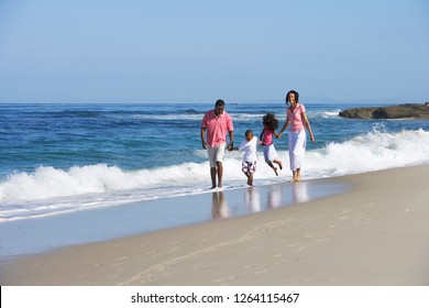 Family walking in surf on sandy beach summer vacation holding hands side by side with waves breaking on shore - Powered by Shutterstock