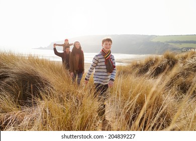 Family Walking Through Sand Dunes On Winter Beach