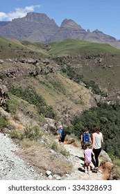 A Family Walks Along A Hiking Trail Under Champagne Castle And Cathkin Peak In The Drakensberg Mountain Range In Rural KwaZulu-Natal, South Africa.