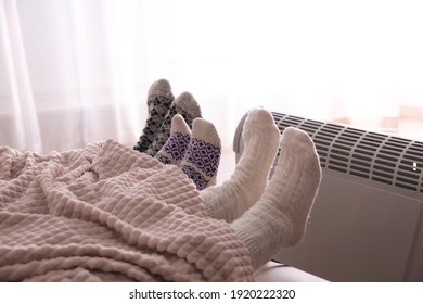 Family Warming Feet Near Electric Heater At Home, Closeup