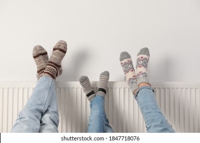 Семейное потепление ног на радиаторе отопления возле белой стены, крупный план
