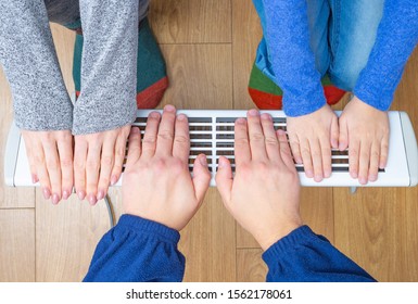 Family Warms His Hands On An Electric Heater At Home. The Symbolic Image Of A House Heating In The Winter Cold Time. 