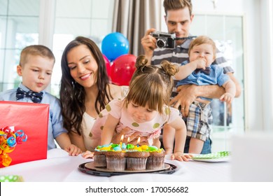 Family Watching Girl Blowing Out Candles On Birthday Cake At Home