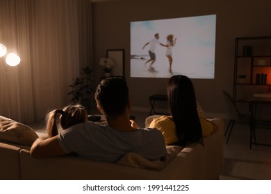 Family watching movie on sofa at night, back view