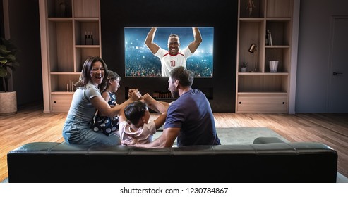 A family is watching a soccer moment on the TV and celebrating a goal, sitting on the couch in the living room. The living room is made in 3D. - Shutterstock ID 1230784867