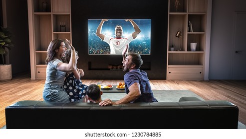 A family is watching a soccer moment on the TV and celebrating a goal, sitting on the couch in the living room. The living room is made in 3D. - Shutterstock ID 1230784885