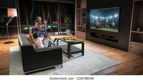A family is watching a soccer moment on the TV and celebrating a goal, sitting on the couch in the living room. The living room is made in 3D. - Shutterstock ID 1230788548