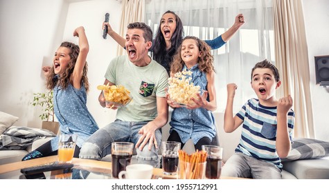 Family Watching Sports Match On Tv At Home, Cheering And Shouting Goal With Hands Up, Spilling Chips And Popcorn From Excitement.