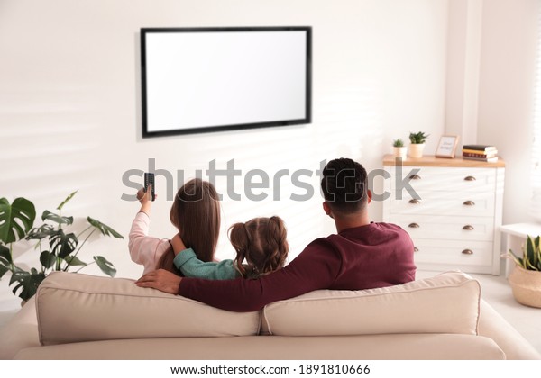 Family watching TV\
on sofa at home, back\
view