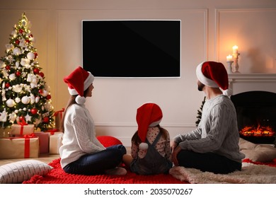 Family Watching TV In Room Decorated For Christmas