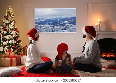 Family Watching TV In Room Decorated For Christmas