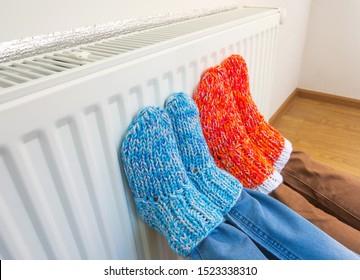 Family Wearing Colorful Pair Of Knitted Wool Socks Warming Cold Feet In Front Of Heating Radiator In Winter Time. Electric Or Gas Heater At Home. The Symbolic Image Of The Heating Season At Home.