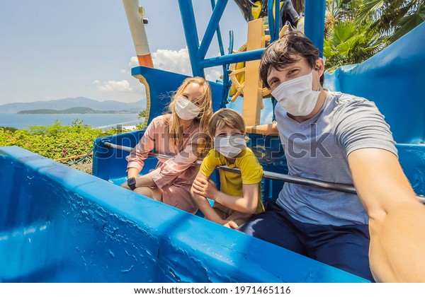 Family wearing a medical mask during COVID-19\
coronavirus at an amusement\
park