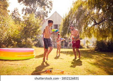 Family Wearing Swimming Costumes Having Water Fight With Water Pistols In Summer Garden