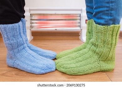 A Family Wearing Woollen Handmade Socks Warms Their Cold Feet At An Electric Heater. Infrared Halogen Heater At Home.