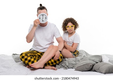 Family Wearing Yellow Plaid Pajamas On White Studio Background. Dad Covering Face With Big Clock Alarm. Preteen Daughter In Eyewear Looks At Camera. Early Morning Wake Up. Daily Routine. Lifestyle 