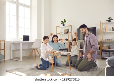 Family Weekend Entertainment. Mom, Dad, Daughter And Son Play Game Sitting At A Table From Which A Wooden Tower Falls. Fun Board Games For Family Leisure. Stay At Home Activity For Kids.