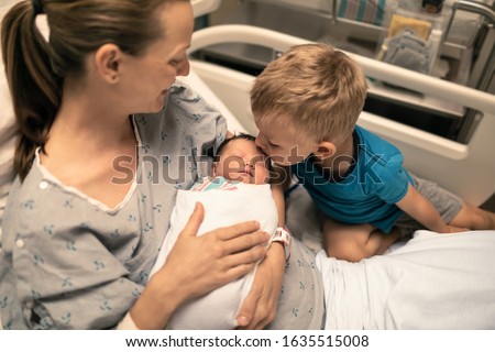 Family welcoming new baby girl into the world.  Mother holding new born baby in hospital and her little brother seeing her for the first time.