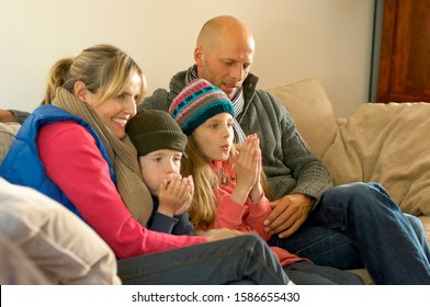 Family In Winter Clothes Keeping Warm Together On Sofa