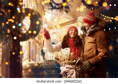 Family, Winter Holidays And Celebration Concept - Happy Mother, Father And Little Daughter At Christmas Market On Town Hall Square In Tallinn, Estonia Over Lights