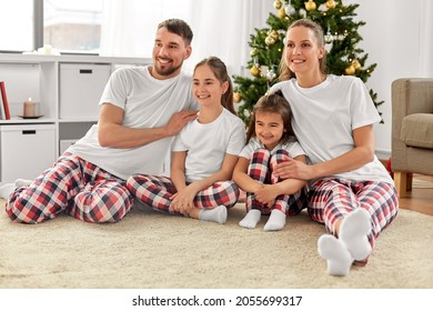 Family, Winter Holidays And Christmas Concept - Happy Mother, Father And Two Daughters In Matching Pajamas Sittin On Floor At Home