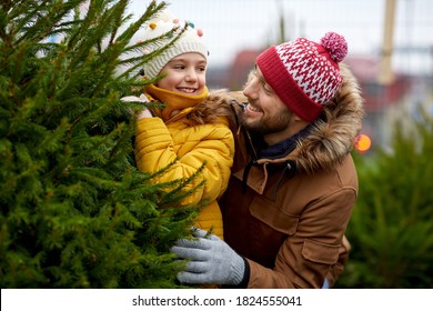 family, winter holidays and people concept - happy father and little daughter choosing christmas tree at street market