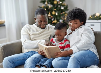 Family, Winter Holidays And People Concept - Happy African American Mother, Father And Little Son Reading Book At Home On Christmas