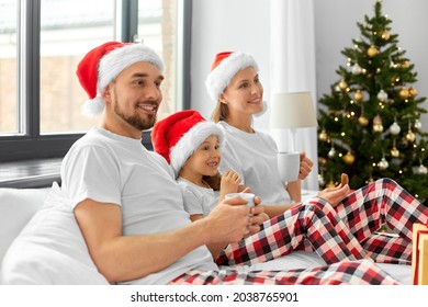 Family, Winter Holidays And People Concept - Happy Mother, Father And Little Daughter With Christmas Gifts Drinking Coffee And Eating Cookies In Bed At Home