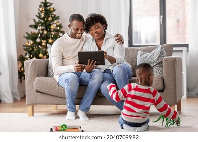 Family, Winter Holidays And People Concept - Happy African American Mother And Father Using Tablet Pc Computer And Baby Son Playing With Toy Blocks And Dinosaur At Home On Christmas