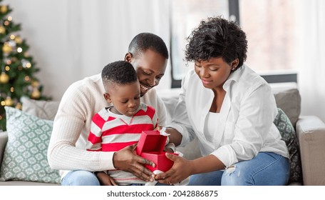 Family, Winter Holidays And People Concept - Happy African American Mother, Father And Baby Son Opening Gift Box At Home On Christmas