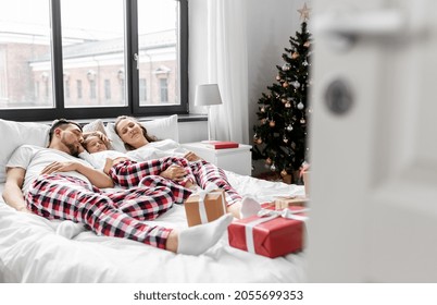 Family, Winter Holidays And People Concept - Happy Little Daughter, Mother And Father In Matching Pajamas Sleeping In Bed On Christmas Morning