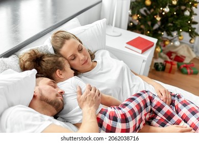 Family, Winter Holidays And People Concept - Happy Little Daughter, Mother And Father In Matching Pajamas Sleeping In Bed On Christmas Morning