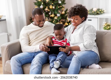 Family, Winter Holidays And People Concept - Happy African American Mother, Father And Baby Son With Tablet Pc Computer At Home On Christmas