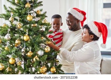 Family, Winter Holidays And People Concept - Happy African American Mother, Father And Little Son Decorating Christmas Tree At Home On