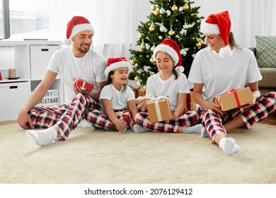 Family, Winter Holidays And People Concept - Happy Mother, Father And Two Daughters In Santa Hats With Christmas Gifts At Home